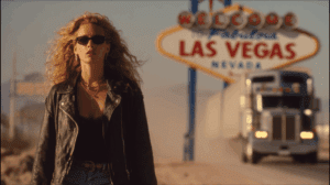 Nomi Malone haciendo autostop en carretera hacia Las Vegas con maleta